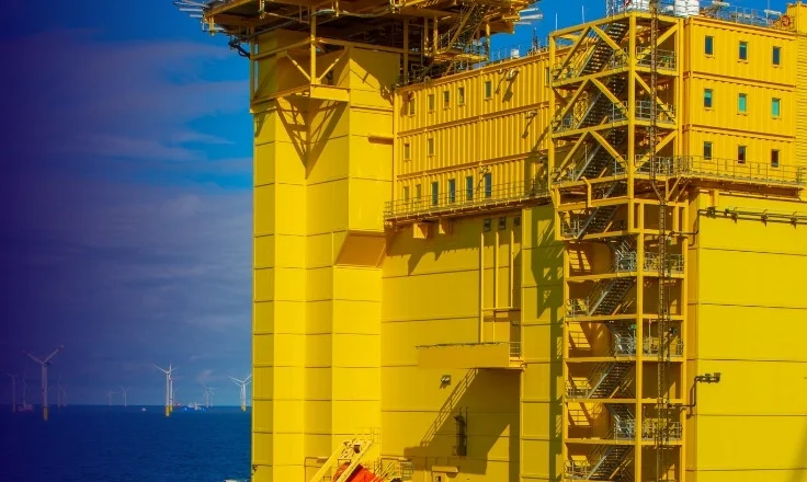 Offshore substation with wind turbines in the background.